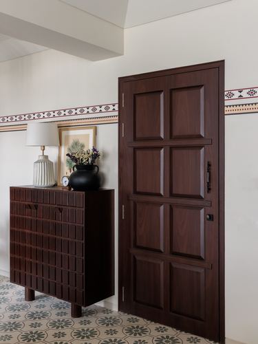 Entryway with dark paneled wooden door, ribbed cabinet, patterned floor tiles and decorative border.