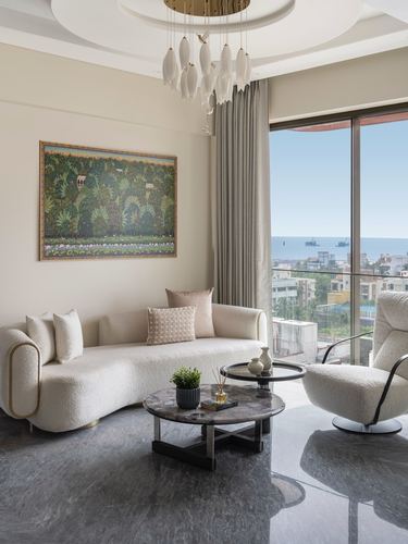 Curved cream sofa and marble table in living room overlooking Mumbai sea view