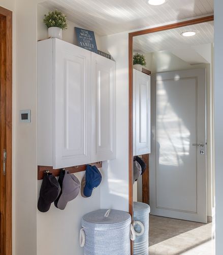 White foyer with wall cabinet, hanging caps, woven basket, and mirror reflecting hallway door