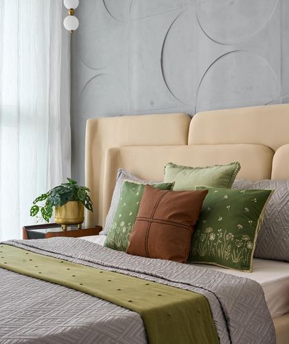 Bed with cream upholstered headboard, green and brown pillows, sculpted grey wall panel behind
