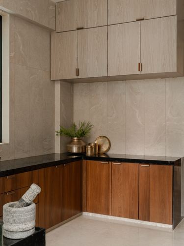 Corner kitchen with stone tile walls, wood-veneer cabinets, black countertop and brass vessels