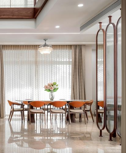 Dining room with long table, orange chairs, sheer curtains and fluted glass room divider