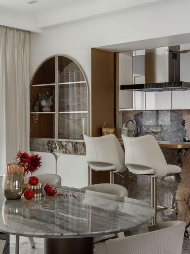 Dining area with round marble table, cream bar stools, and arched marble niche cabinet leading to kitchen