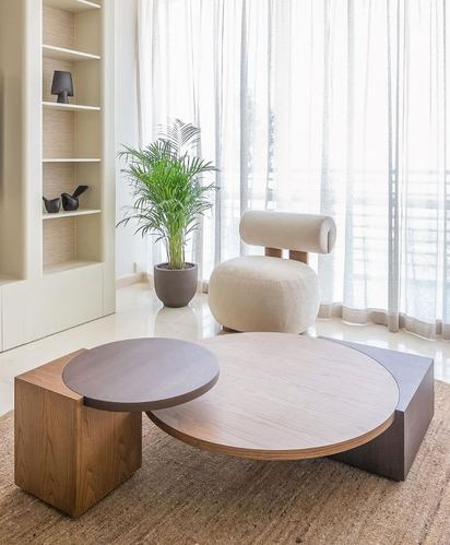 Living room corner with two overlapping round wood coffee tables, bouclé chair, palm plant and sheer curtains