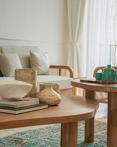 Close-up of wooden coffee table with vases and books beside a cane-armed sofa in a bright living room