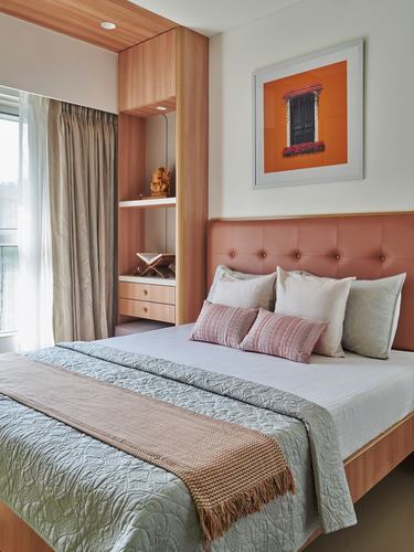 Bedroom with terracotta tufted headboard, wooden niche shelving, and framed orange window photograph on wall