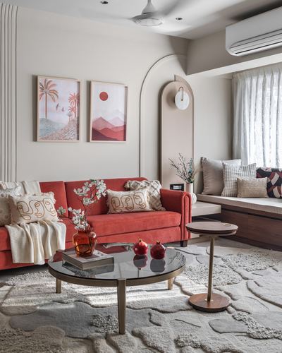 Coral velvet sofa in a beige living room with arched niche, gallery art, and round glass coffee table