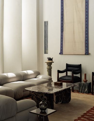 Living room corner with grey sofa, marble coffee table, black leather chair, and hanging textile scroll