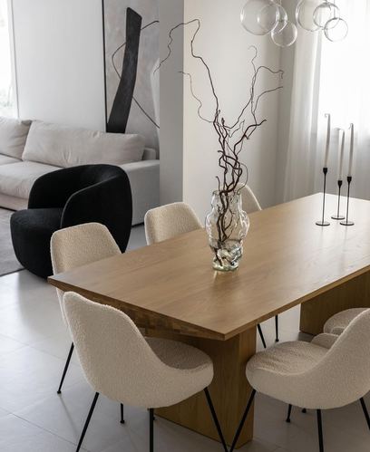 Wooden dining table with boucle chairs, glass vase of branches, and bubble chandelier above