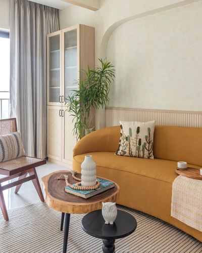 Mustard curved sofa in sunlit living room with wooden cabinet and rattan chair, Mumbai apartment