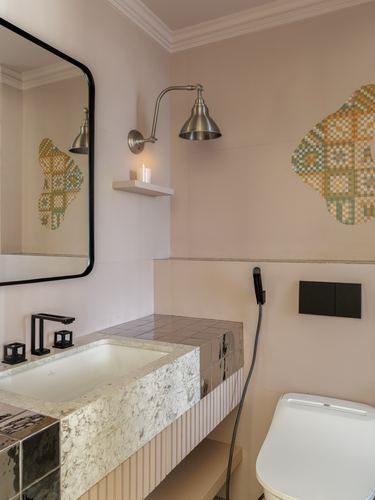 Pink-toned bathroom with stone vanity, black mirror, metal sconce and mosaic wall art