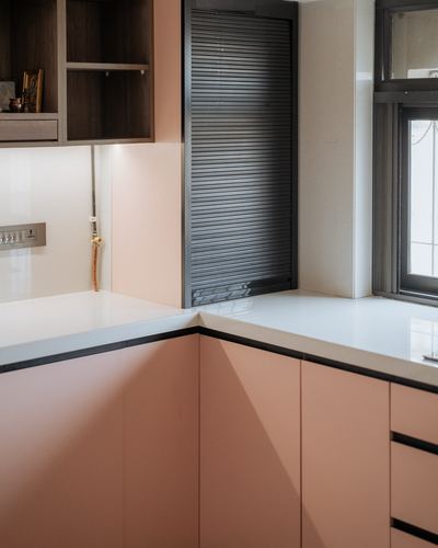 L-shaped blush pink kitchen counter meeting a dark rolling shutter panel near a window