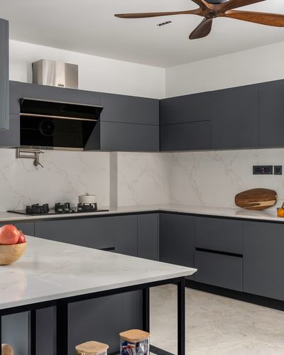 L-shaped dark grey kitchen with white veined countertop, chimney hood, and wooden ceiling fan overhead