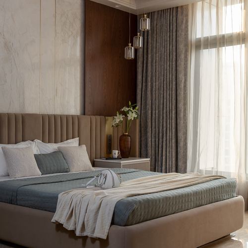 Beige upholstered bed with sage throw, marble headboard wall, wood panel, sheer curtains and pendant lights