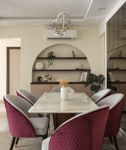 Dining room with marble table, burgundy velvet chairs, and arched wall niche with shelves