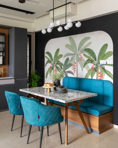 Dining nook with teal banquette, arched banana leaf mural, and terrazzo table with quilted chairs