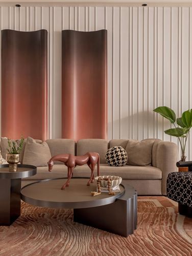 Beige sofa with terracotta horse sculpture on round coffee tables before ombre bronze wall panels