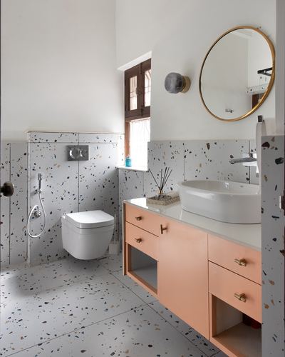 Bathroom with terrazzo walls, peach vanity, vessel sink, round brass mirror, and wall-hung toilet