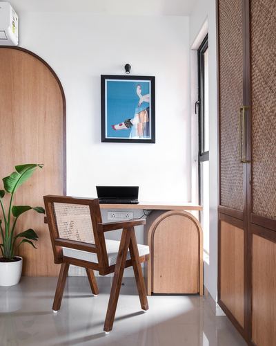 Study nook with cane chair, wooden desk, arched door, and framed art on white wall