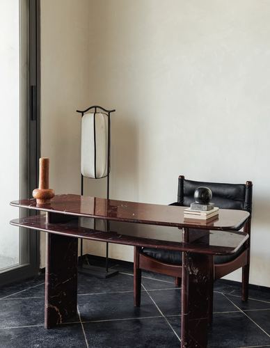 Deep red marble desk with black leather chair beside a floor lamp in a plastered corner