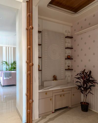 Pooja unit with carved om panel, corner shelves, and leaf-print wallpaper in Jaipur home