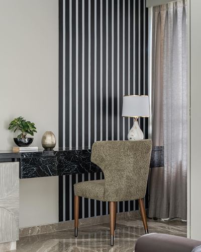 Striped black and white wall behind marble console with lamp and boucle armchair