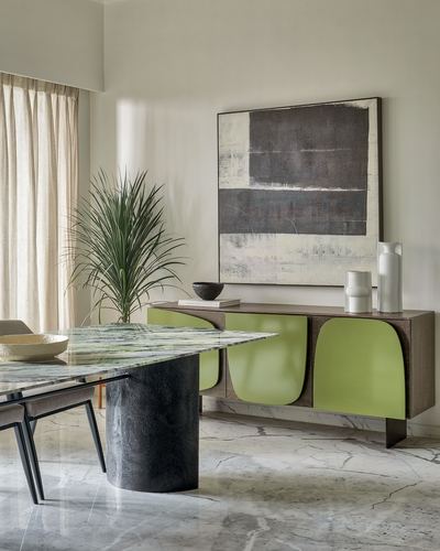 Dining room with green marble table, dark cylindrical base, and green curved sideboard below abstract art