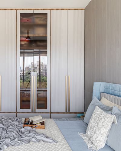 Bedroom with fluted wardrobes, mirrored panel reflecting city view, blue tufted bed with cushions