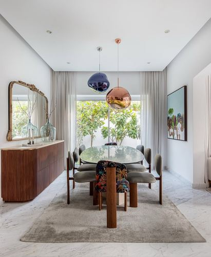 Dining room with glass oval table, grey chairs, fluted wood sideboard and arched mirror