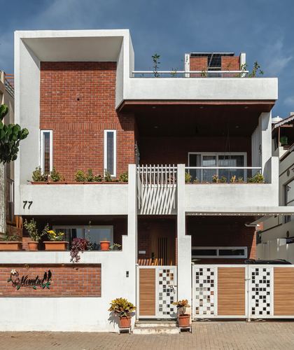 Three-storey brick and white concrete house facade with wooden gate and rooftop garden under blue sky