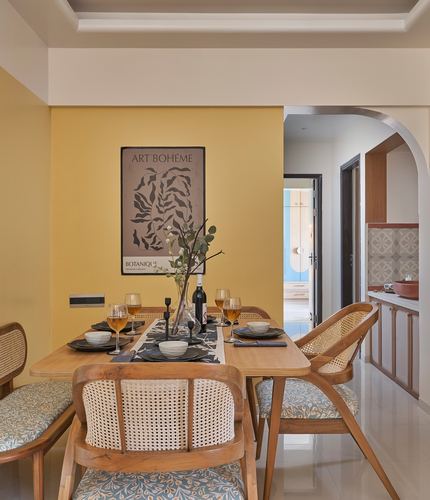 Dining table set with cane chairs against a mustard wall with framed art print