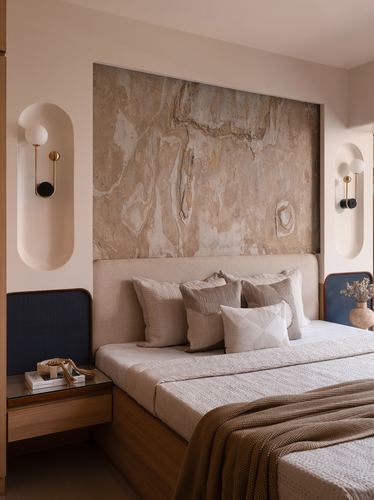 Bedroom with stone slab feature wall, upholstered headboard, and paired oval wall sconces