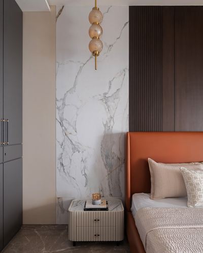 Bedroom corner with marble accent wall, orange leather headboard, and layered globe pendant light