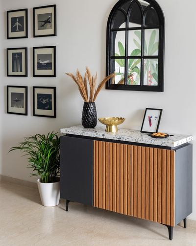 Sideboard with terrazzo top, fluted wood door, arched black mirror and gallery wall of airplane photos above