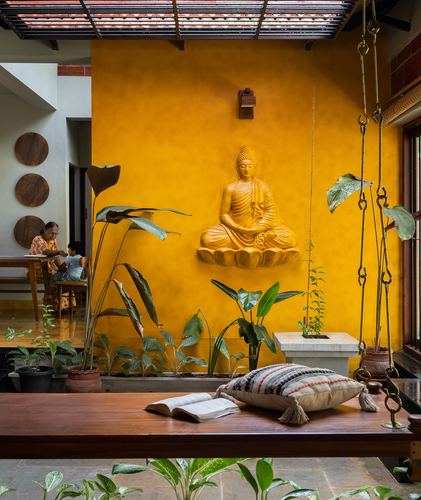 Mustard wall with carved buddha relief above a wooden swing seat and courtyard plants