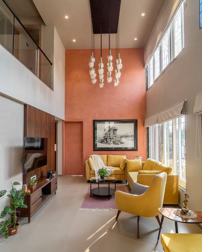 Double-height living room with terracotta wall, cluster chandelier, and mustard yellow sofas