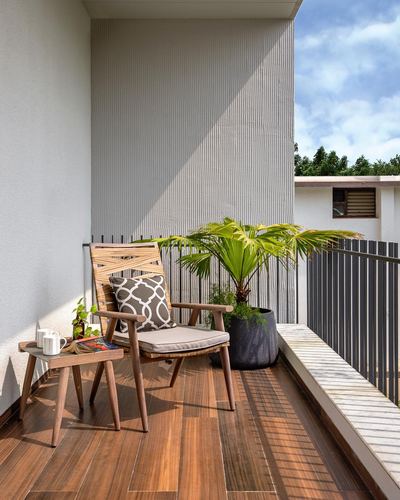 Balcony corner with wooden armchair, side table, potted palm, and striped wall panel under blue sky