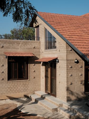 Stone-textured farmhouse facade with terracotta tiled gable roof and wooden door under clear sky