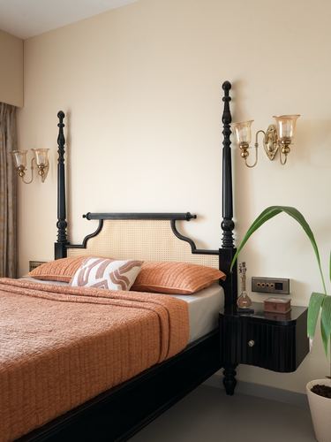 Black four-poster bed with cane headboard, terracotta bedding, and brass wall sconces in a warm bedroom