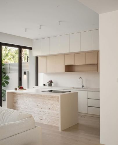Minimalist neutral kitchen with stone-clad island, wood-toned upper cabinets, and glass doors to garden