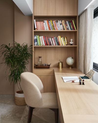 Built-in wooden bookshelf and L-shaped desk in a sunlit study corner with an upholstered chair