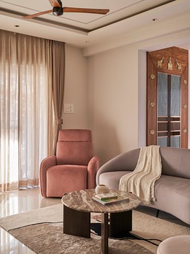 Living room with dusty pink recliner, curved grey sofa, round marble coffee table, and carved wooden niche