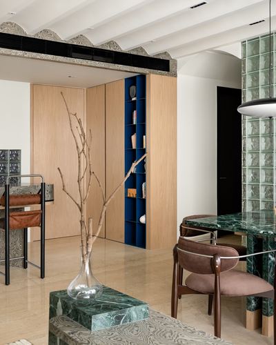 Mumbai apartment vignette with wood beams, marble dining table, glass block column and built-in oak bookshelf
