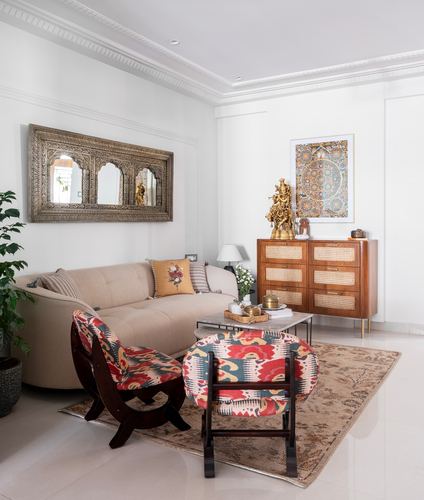 Living room with cane cabinet, brass Krishna statue, arched mirror, patterned x-frame chairs and rug