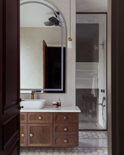 Bathroom with arched mirror, fluted wood vanity, vessel sink, and glass shower visible through open door