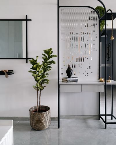 Foyer with perforated metal screen console, mirror, plant in woven basket, on grey stone floor.