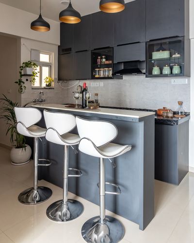 Black kitchen with white bar counter, three white swivel stools, and pendant lights above