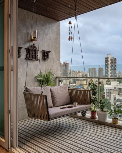 Rope-hung wooden swing with cushions on a balcony overlooking the Mumbai skyline.