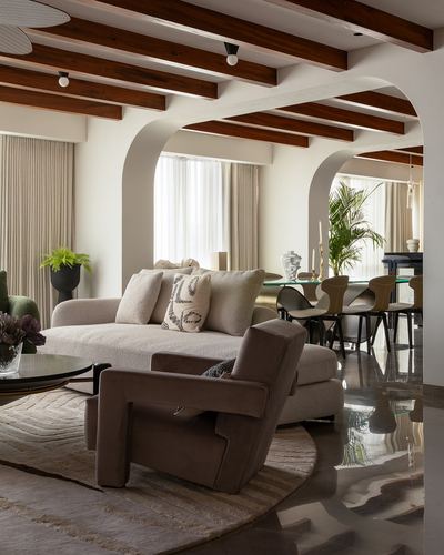 Living room with arched openings, wood beam ceiling, boucle sofa and velvet armchair on polished floor