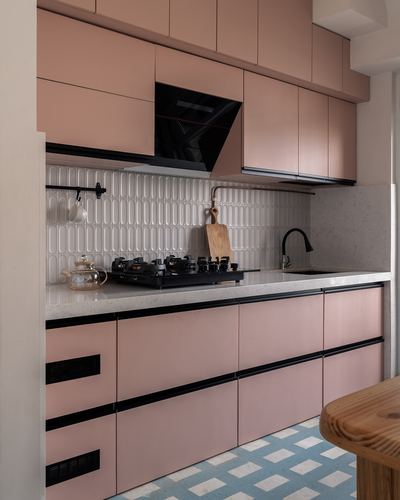 Pastel pink kitchen with black hob, textured white backsplash, and patterned floor tiles